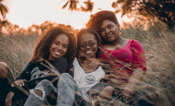 three young Black women sitting together and smiling outdoors