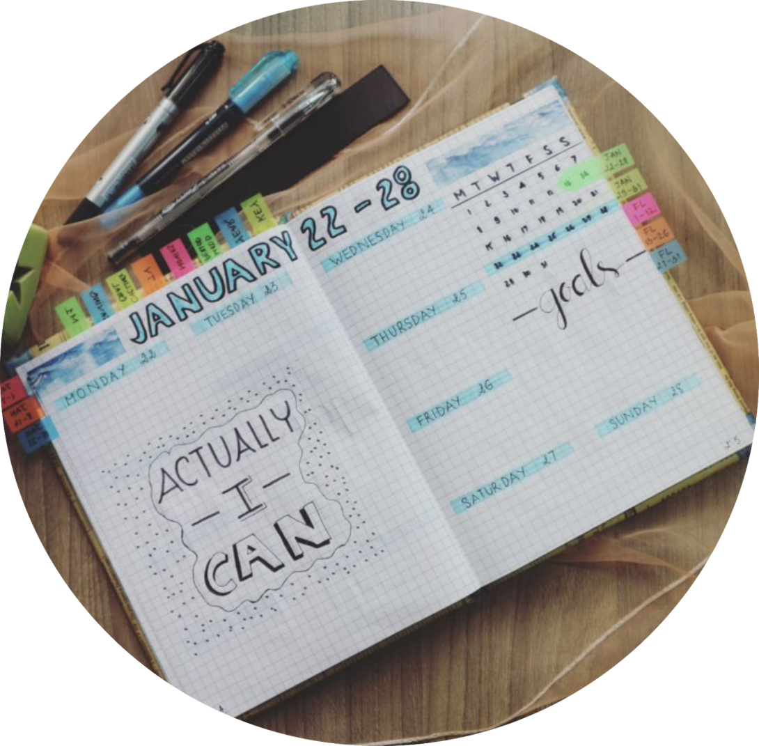 A weekly planner is open on a wooden desk. Large handwritten letters on the left hand side read 
